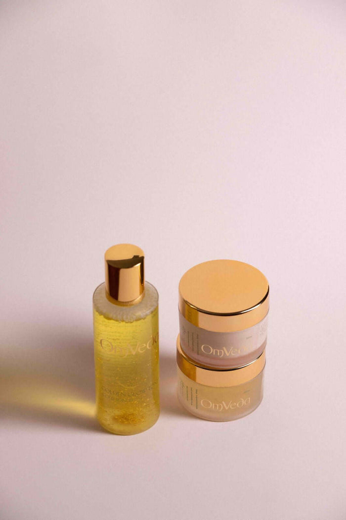 OmVeda yellow skincare bottle with pump and two small gold-lidded jars