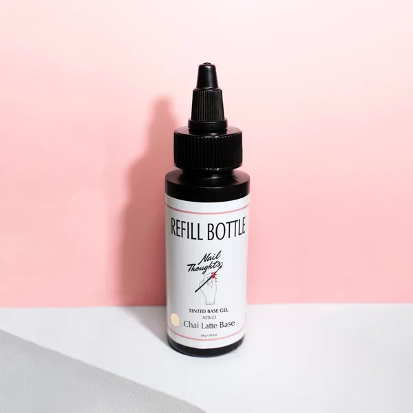 A small bottle labeled 'Refill Bottle' with a black dropper, filled with powdered chai lattes base, positioned against a pink background.