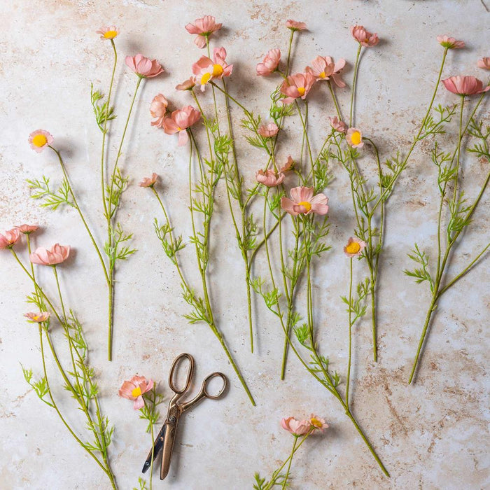 Pink flowers with green stems on a textured surface with a pair of scissors.