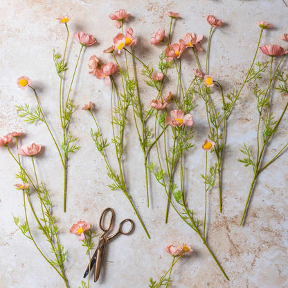 Pink flowers with green stems on a textured surface with a pair of scissors.