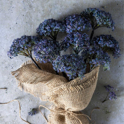 Bouquet of purple flowers in a burlap bag on a textured surface