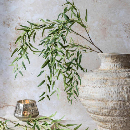 Decorative setting with green branches, a textured vase, and a candle on a light background