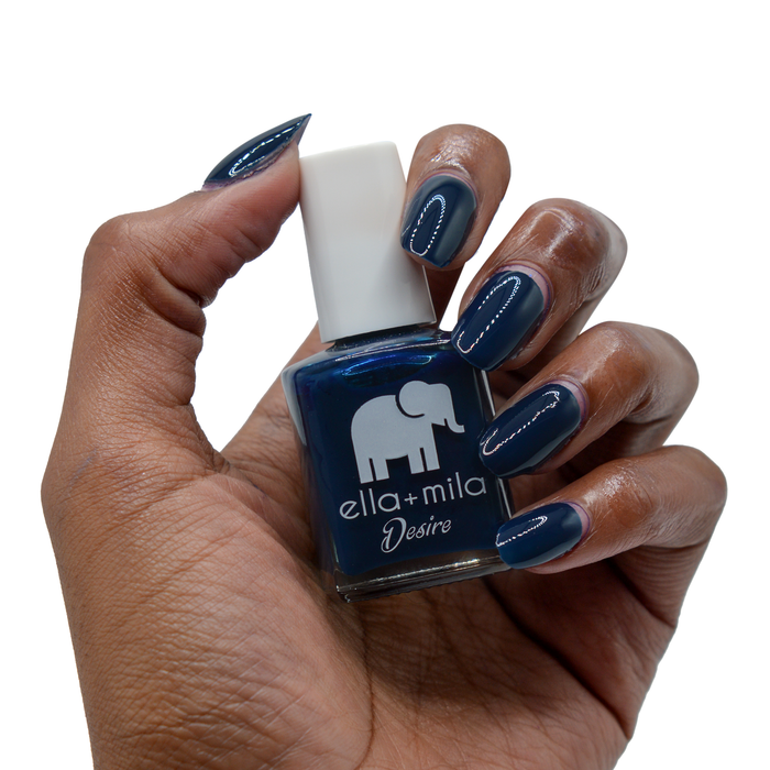 Blindfold Me navy blue nail polish on a deep skin tone, hand holding the bottle