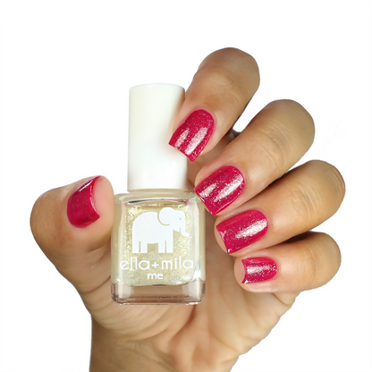 Dipped in Gold shimmer nail polish over a magenta manicure on a medium skin tone, holding the bottle