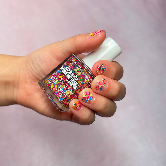 Gabby's Dollhouse rainbow confetti glitter nail polish on a light skin tone, hand holding the bottle