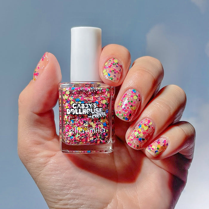 Gabby's Dollhouse confetti glitter nail polish manicure on a medium skin tone, holding the bottle