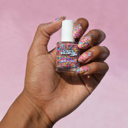 Gabby's Dollhouse rainbow confetti glitter nail polish on a deep skin tone, hand holding the bottle