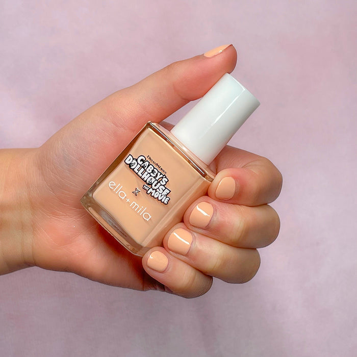 Gabby's Dollhouse peach nail polish on a light skin tone, hand holding the bottle