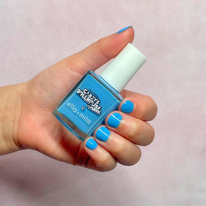 Gabby's Dollhouse sky blue nail polish on a light skin tone, hand holding the bottle