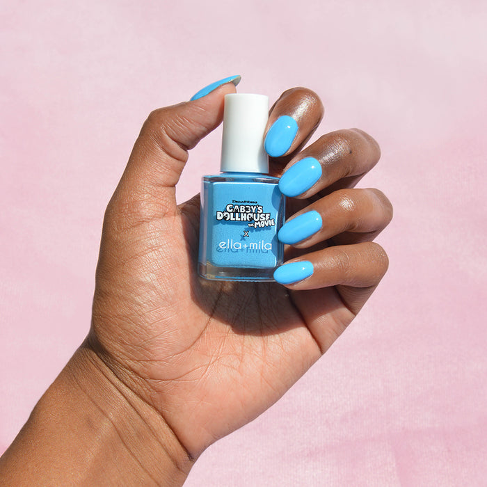 Gabby's Dollhouse sky blue nail polish on a deep skin tone, hand holding the bottle