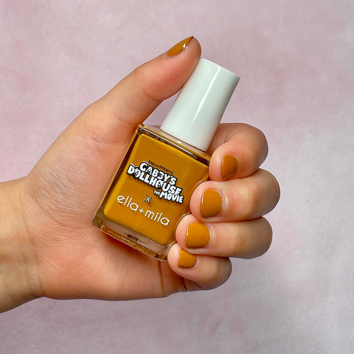 Gabby's Dollhouse caramel brown nail polish on a light skin tone, hand holding the bottle