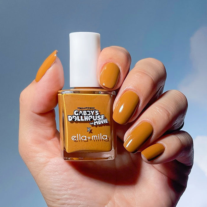 Gabby's Dollhouse caramel brown nail polish manicure on a medium skin tone, holding the bottle