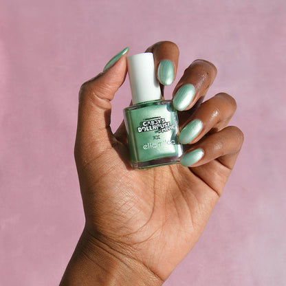 Gabby's Dollhouse mint green shimmer nail polish on a deep skin tone, hand holding the bottle
