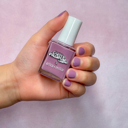 Gabby's Dollhouse lilac shimmer nail polish on a light skin tone, hand holding the bottle