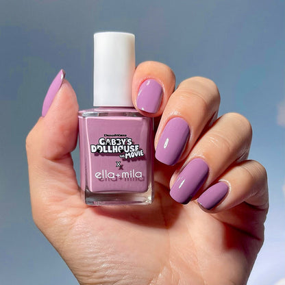 Gabby's Dollhouse lilac shimmer nail polish manicure on a medium skin tone, holding the bottle