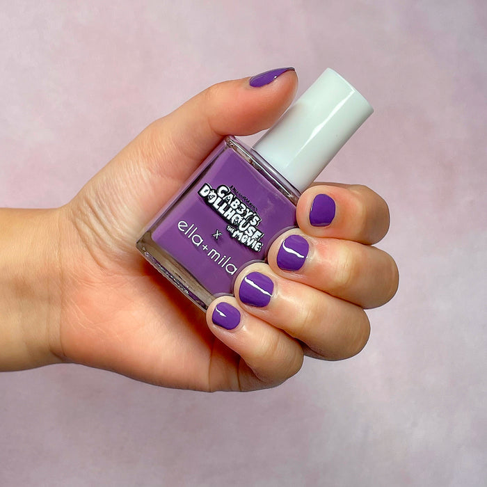 Gabby's Dollhouse purple nail polish on a light skin tone, hand holding the bottle
