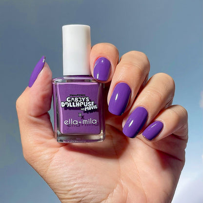 Gabby's Dollhouse purple nail polish manicure on a medium skin tone, holding the bottle