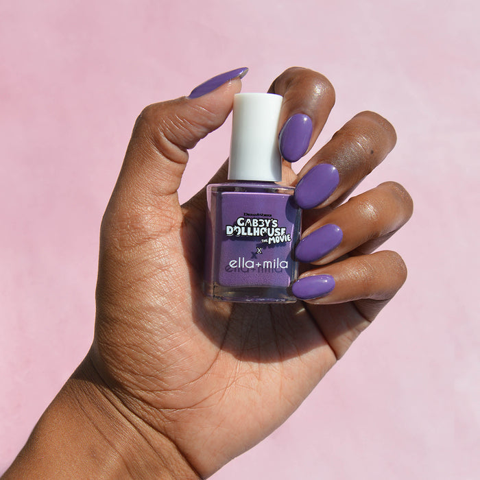Gabby's Dollhouse purple nail polish on a deep skin tone, hand holding the bottle