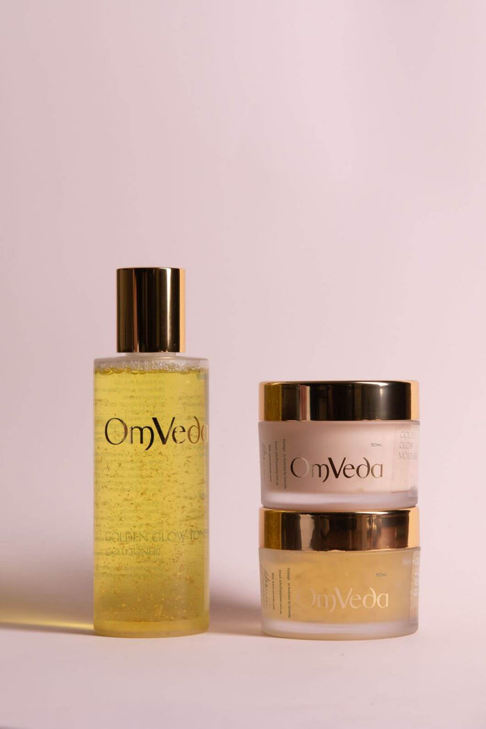 OmVeda golden skincare bottle and matching two-piece cream jars with gold caps