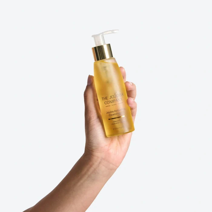 Hand holding a bottle of The Jojoba Company against a white background