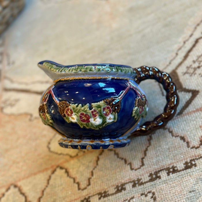 Decorative blue ceramic creamer with floral patterns on a textured surface