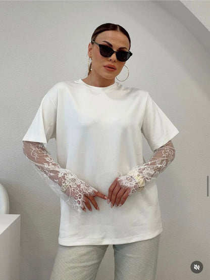 Person wearing a white oversized t-shirt with lace sleeves against a plain background