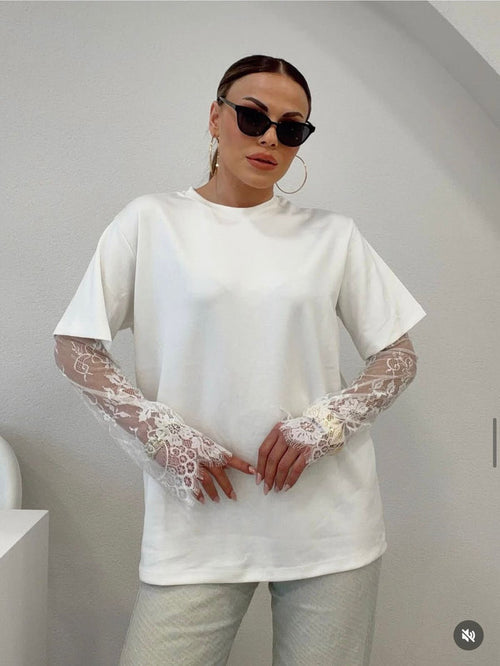 Person wearing a white oversized t-shirt with lace sleeves against a plain background