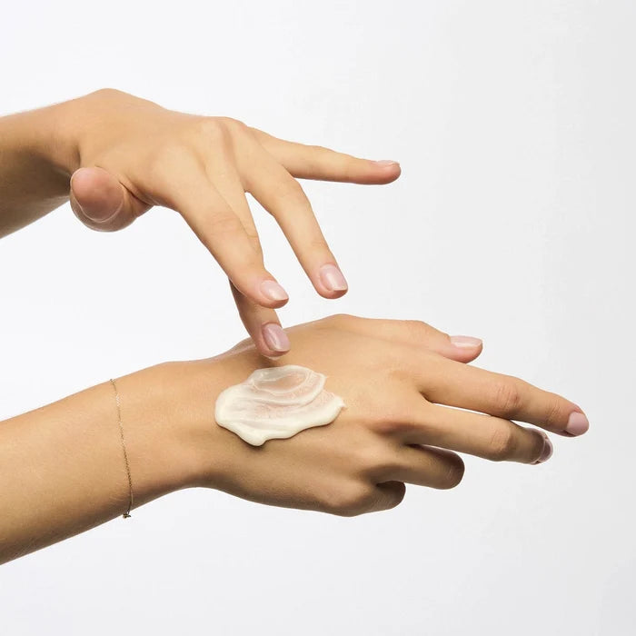 Hand applying cream to another hand on a white background