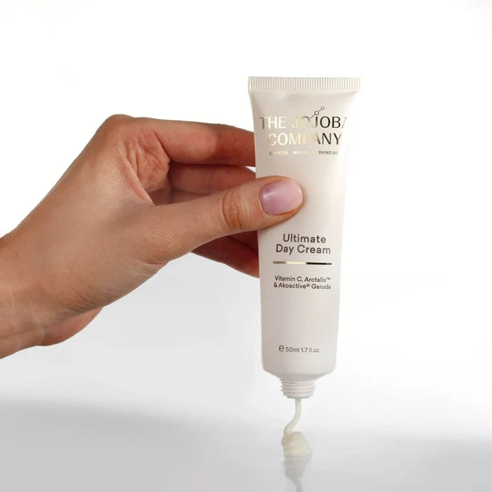 Hand holding a tube of 'The Body Company Ultimate Day Cream' with a white background