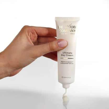 Hand holding a tube of 'The Body Company Ultimate Day Cream' with a white background
