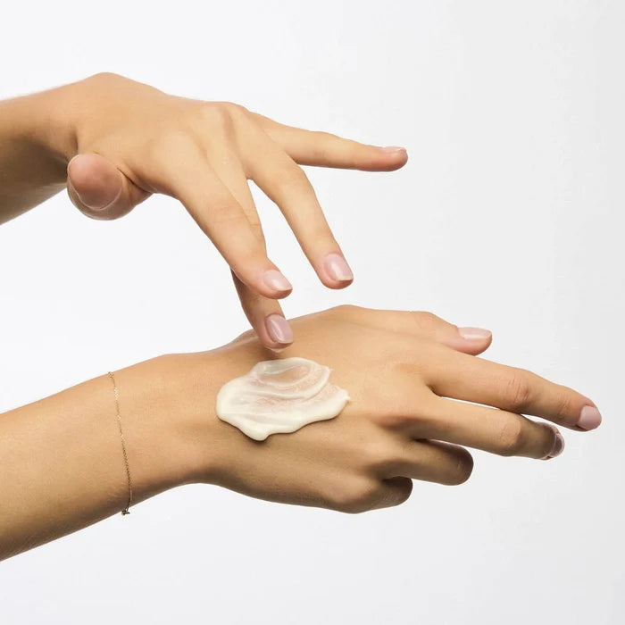 Hand applying ultimate night cream to another hand on a white background