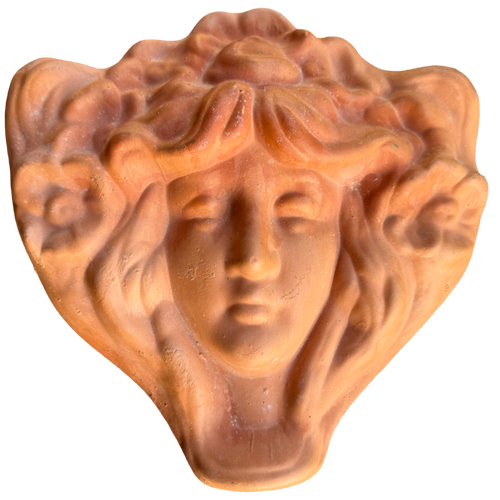 Terracotta sculpture of a face with flowing hair on a white background