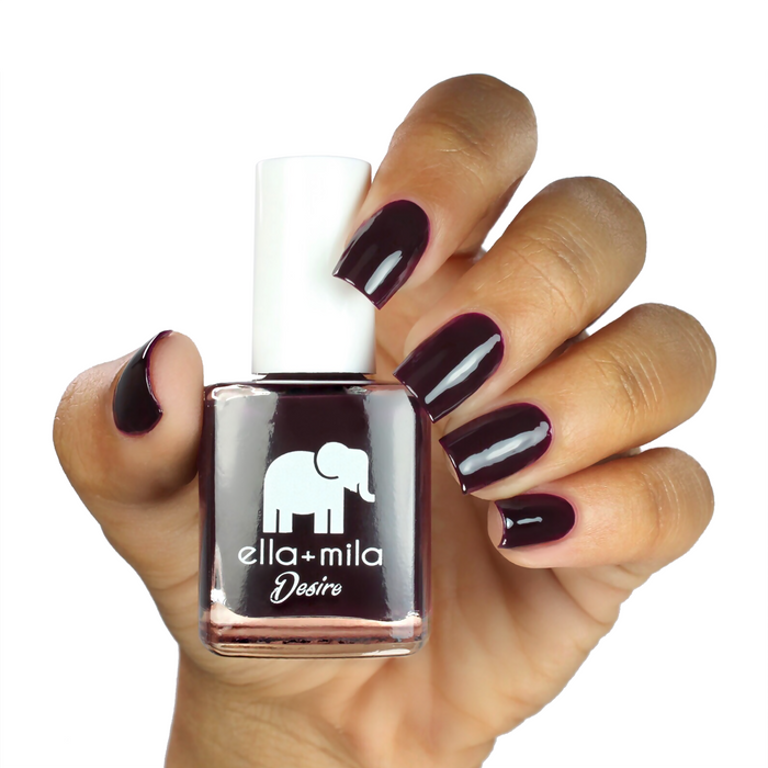 Wine Me Up deep wine nail polish on a medium skin tone, hand holding the bottle