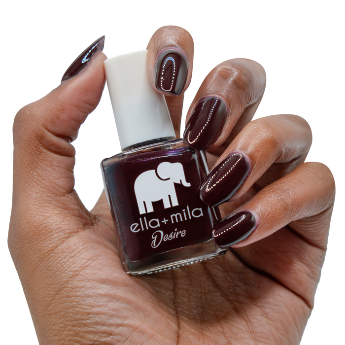 Wine Me Up deep wine nail polish on a deep skin tone, hand holding the bottle